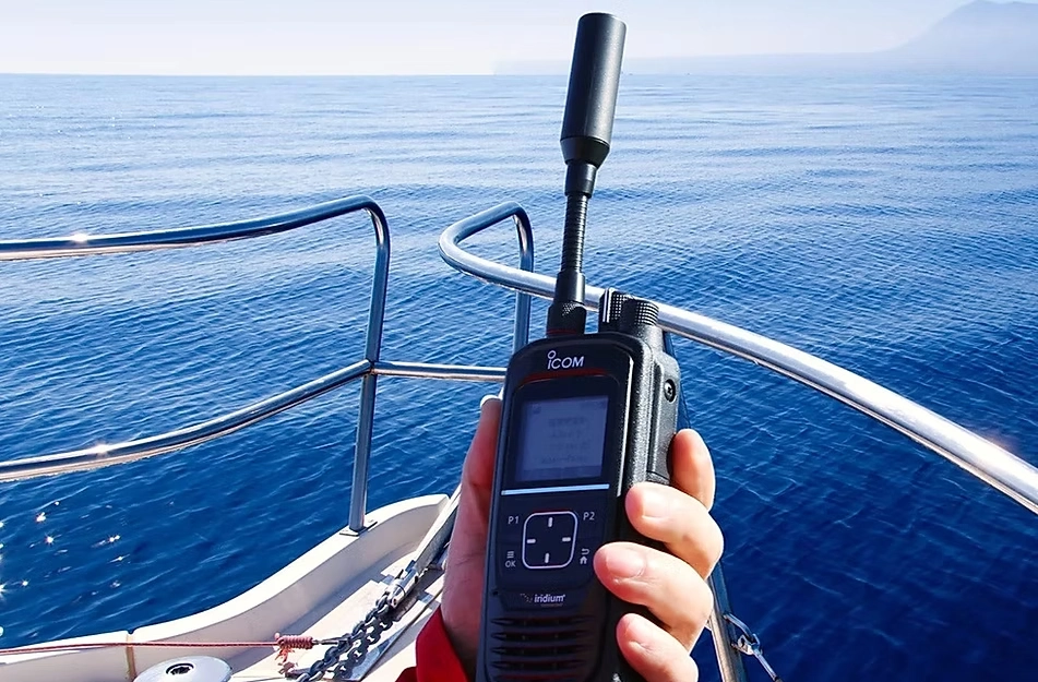 A person holding an ICOM satellite radio on a boat, with the ocean in the background.